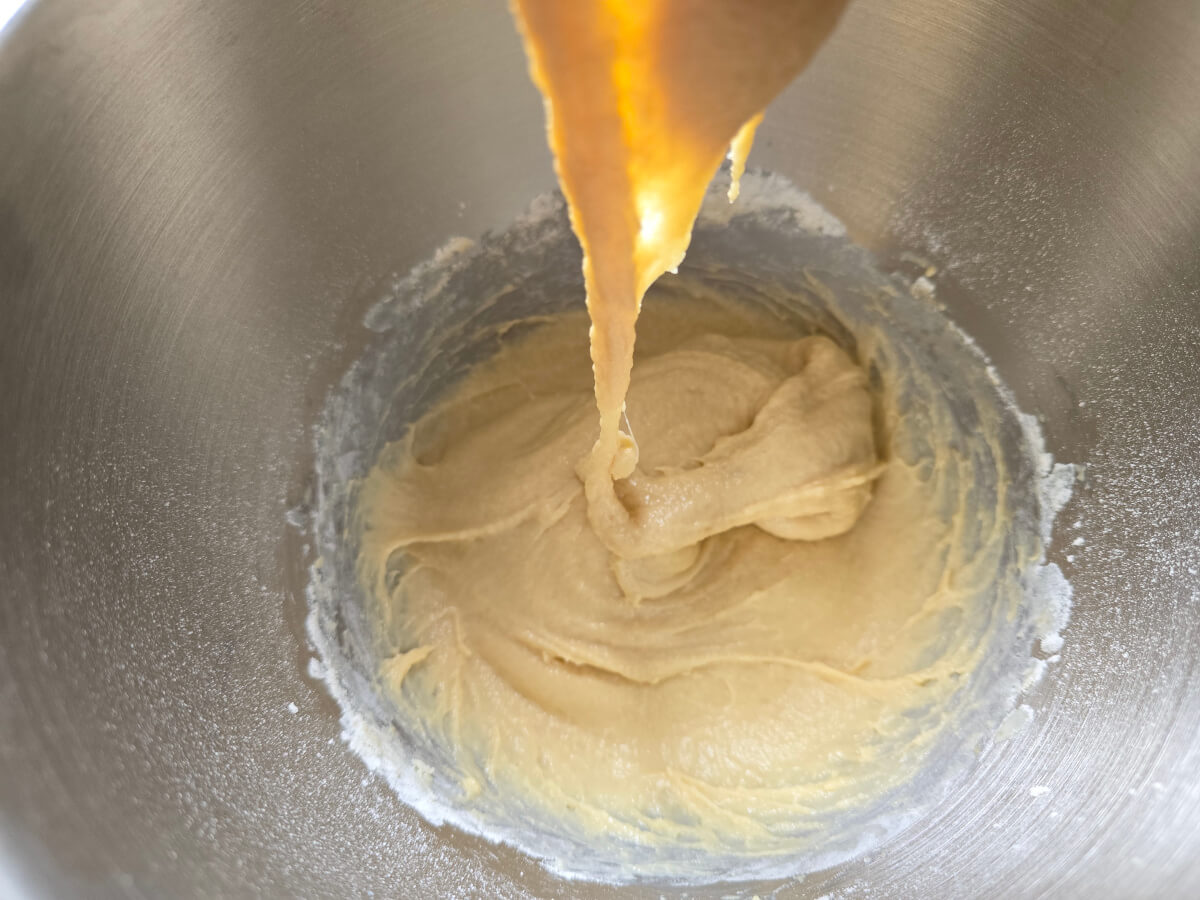 Mélange d'ingrédients ressemblant a une pâte dans la cuve d'un robot pâtissier.